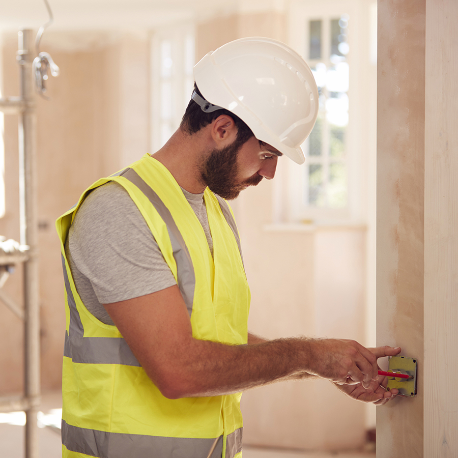 Electrician Wearing Hard Hat Fitting Light Switch At New Build Property